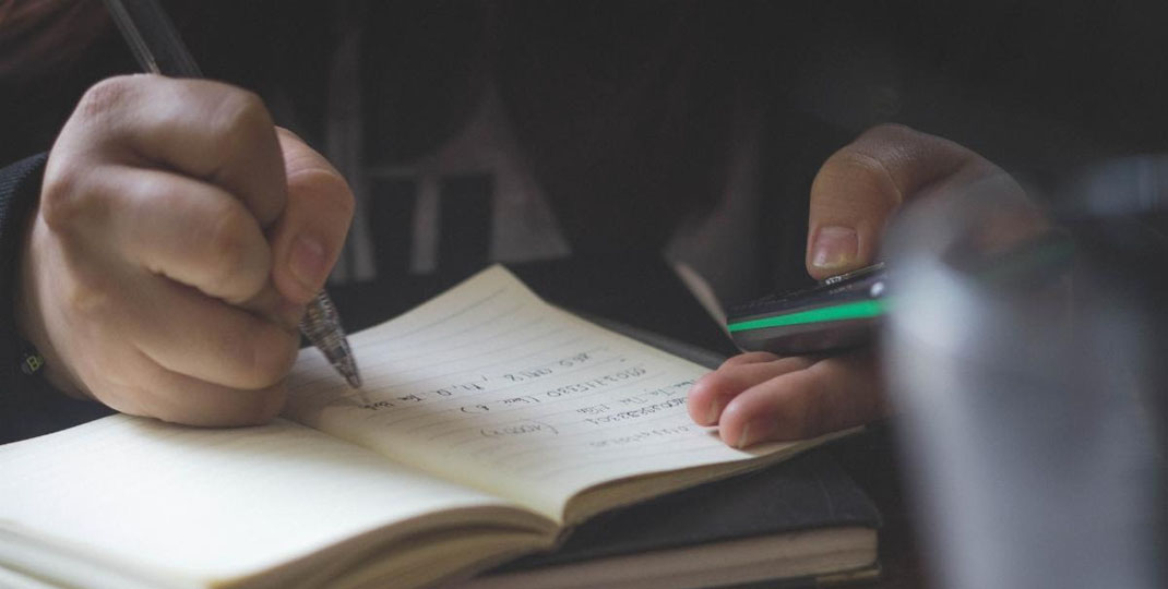 student taking notes and using a calculator