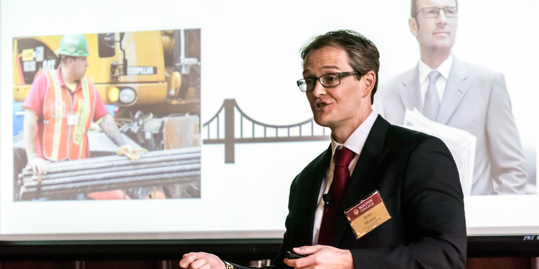 Sean Martin presenting in front of a screen with images of workers projected on it