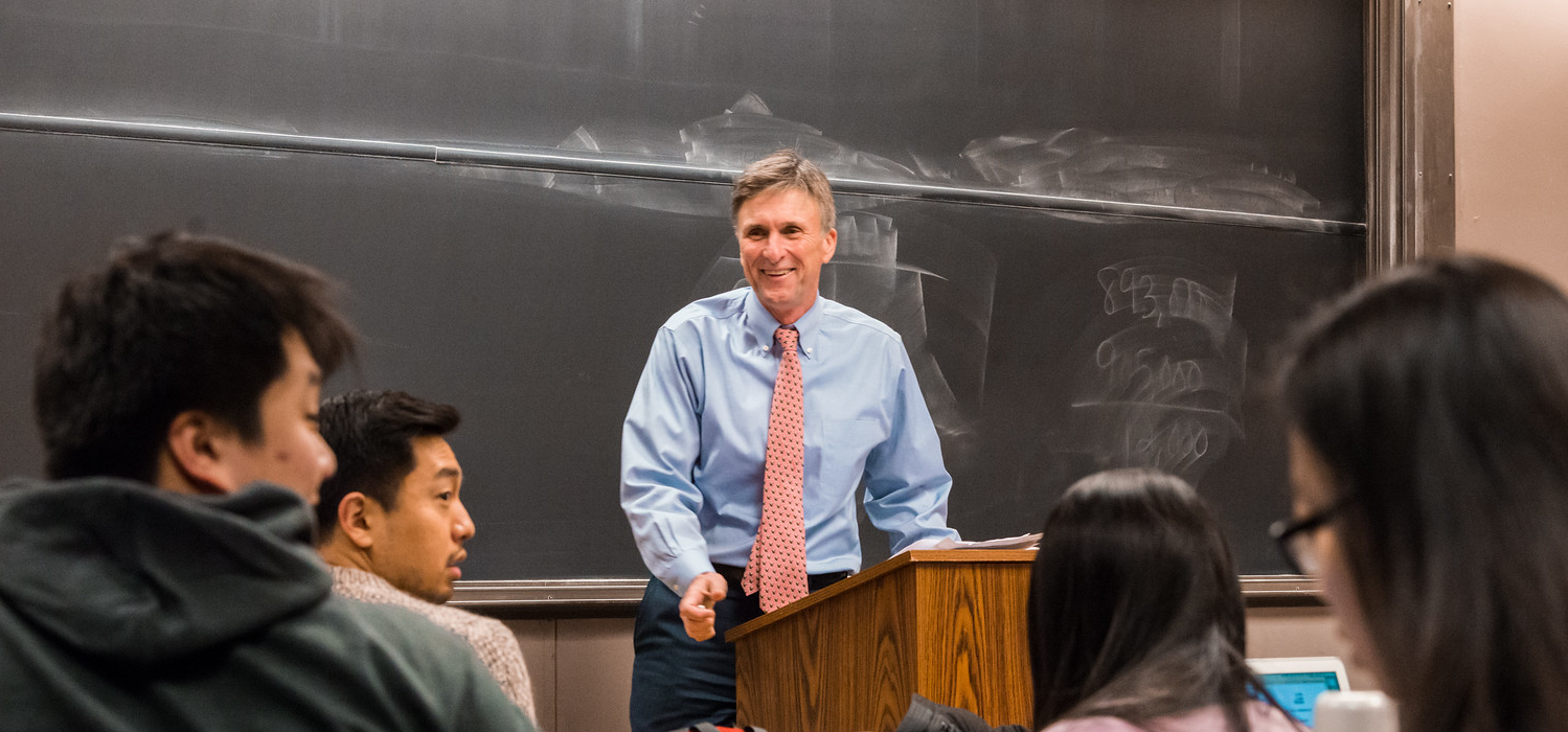 Ed Taylor standing and smiling at a lectern in front of students