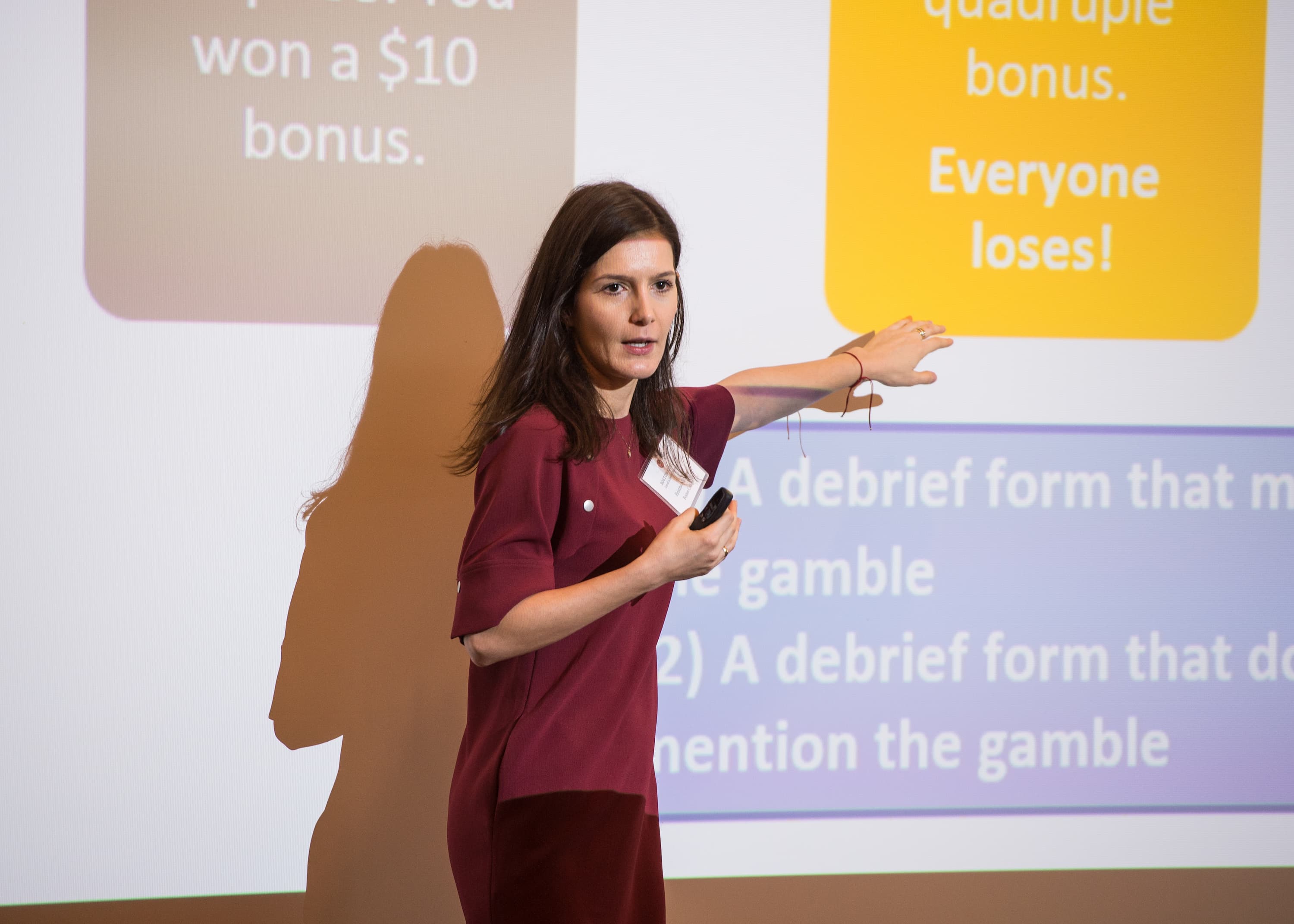 A woman presenting in front of a projection on a board. She is pointing at a text box describing a study