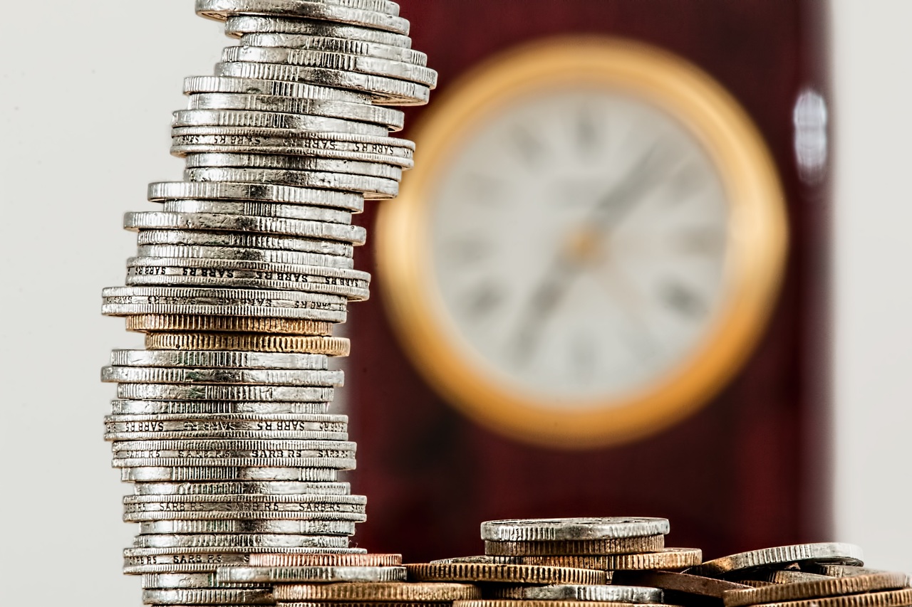 a stack of coins in front of a clock