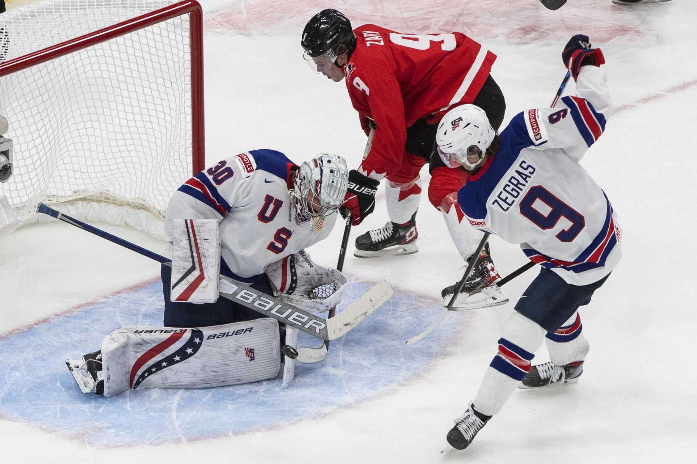 Hockey goalie Spencer Knight makes a dramatic save as two other players look on