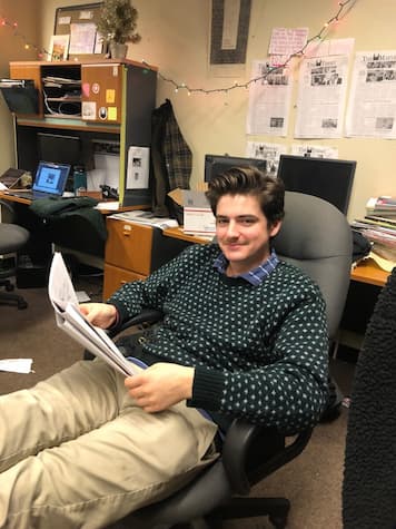 Image of BC alum Timmy Facciola sitting in an office chair while holding a newspaper