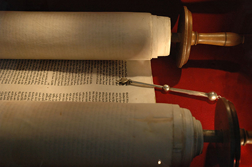 A scroll written in Hebrew resting on a red table
