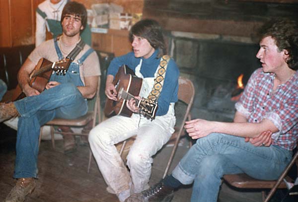 Two seated students playing guitars and another looking on