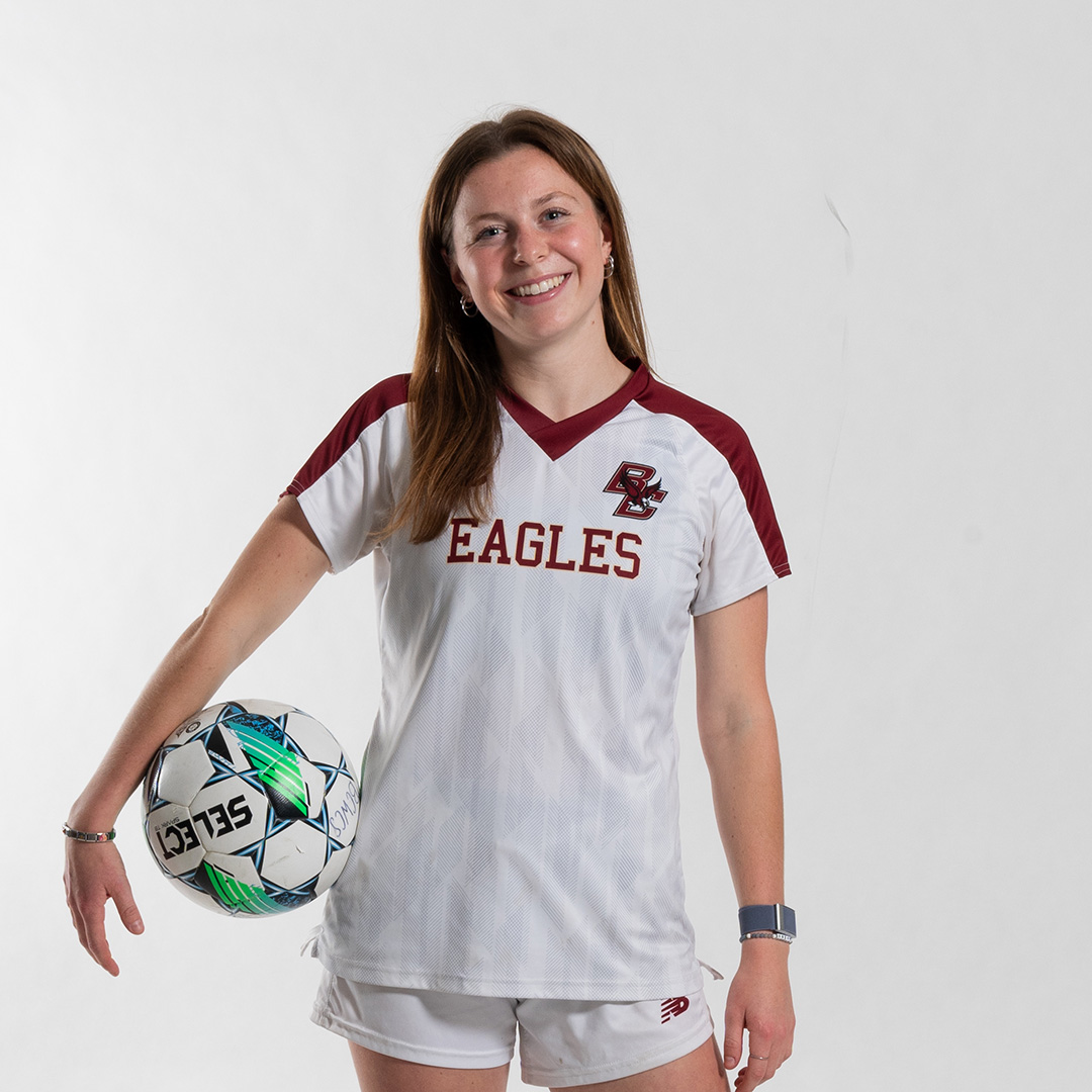 A woman in a BC uniform holding a soccer ball under her arm