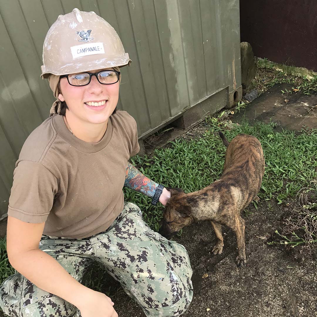 A woman wearing a hardhat petting a dog
