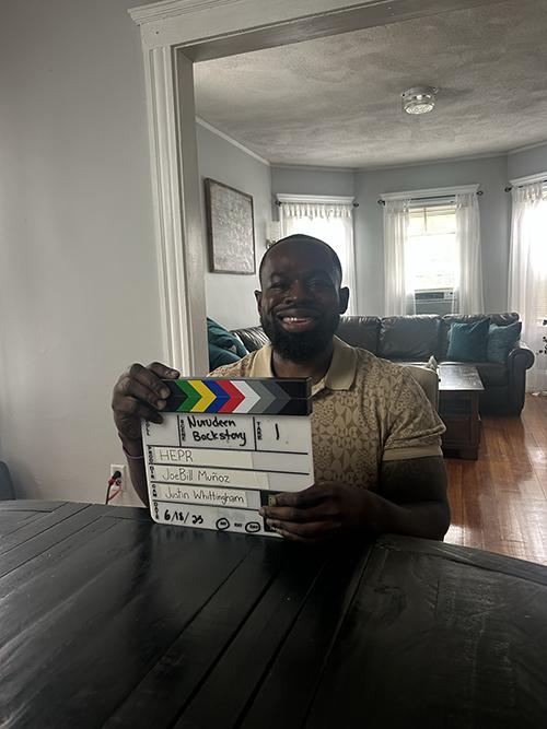 A man sitting at a table holding a clapperboard 