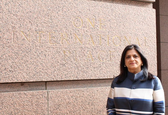 Monica Chandra in a striped sweater in front of a stone wall