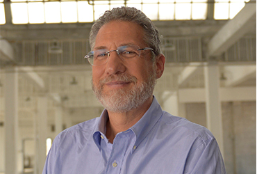 Jonathan F. P. Rose, a gray haired white man with glasses poses indoors